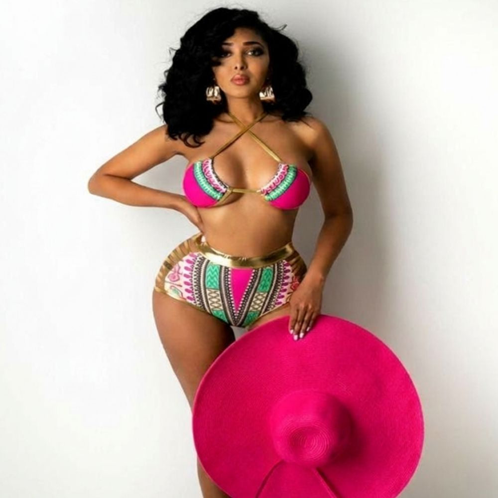 Woman in a colorful bikini holding a large pink hat against a white background