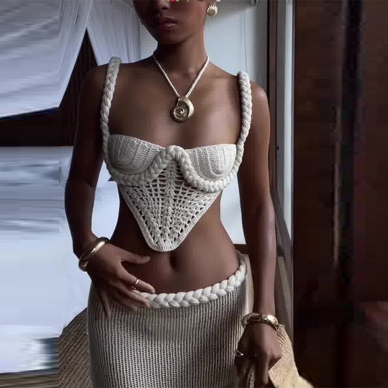 "Model wearing a white crochet knit two-piece set featuring a square-neck crop camisole top with thick straps and a high-waisted ribbed maxi skirt, holding a woven bag in a bedroom setting."