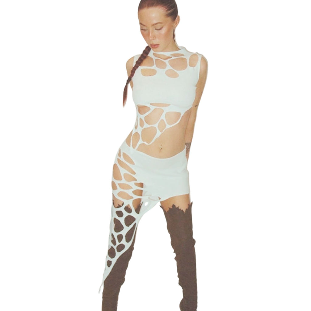 Model with braided hair wearing a bold avant-garde white outfit featuring multiple strategic cut-outs and web-like lattice patterns across the sleeveless top and high-low skirt. Styled with dark brown thigh-high boots, shown in a confident three-quarter pose on a clean studio background.