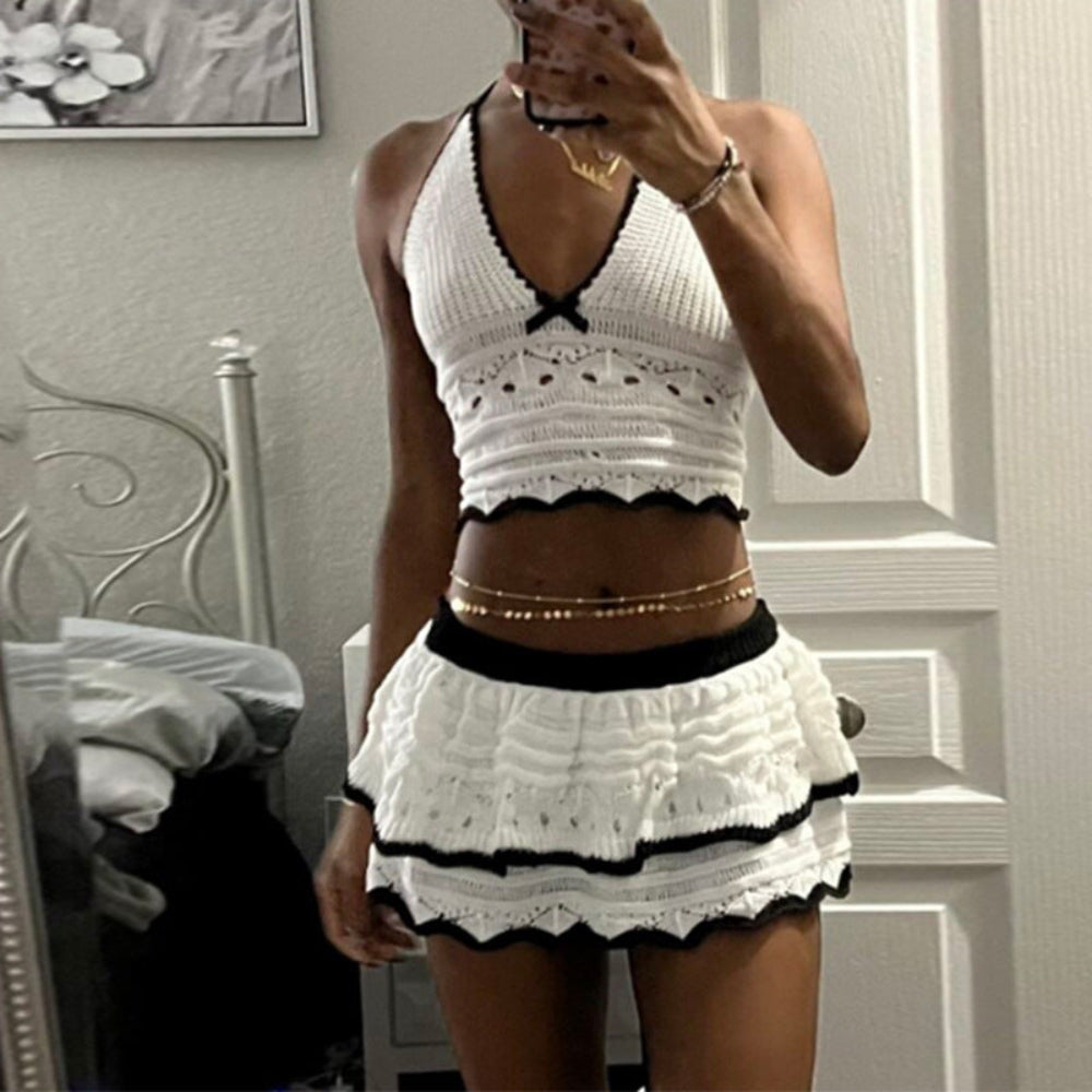 Model in white and black crochet halter crop top and ruffled mini skirt with gold body chain taking mirror selfie.