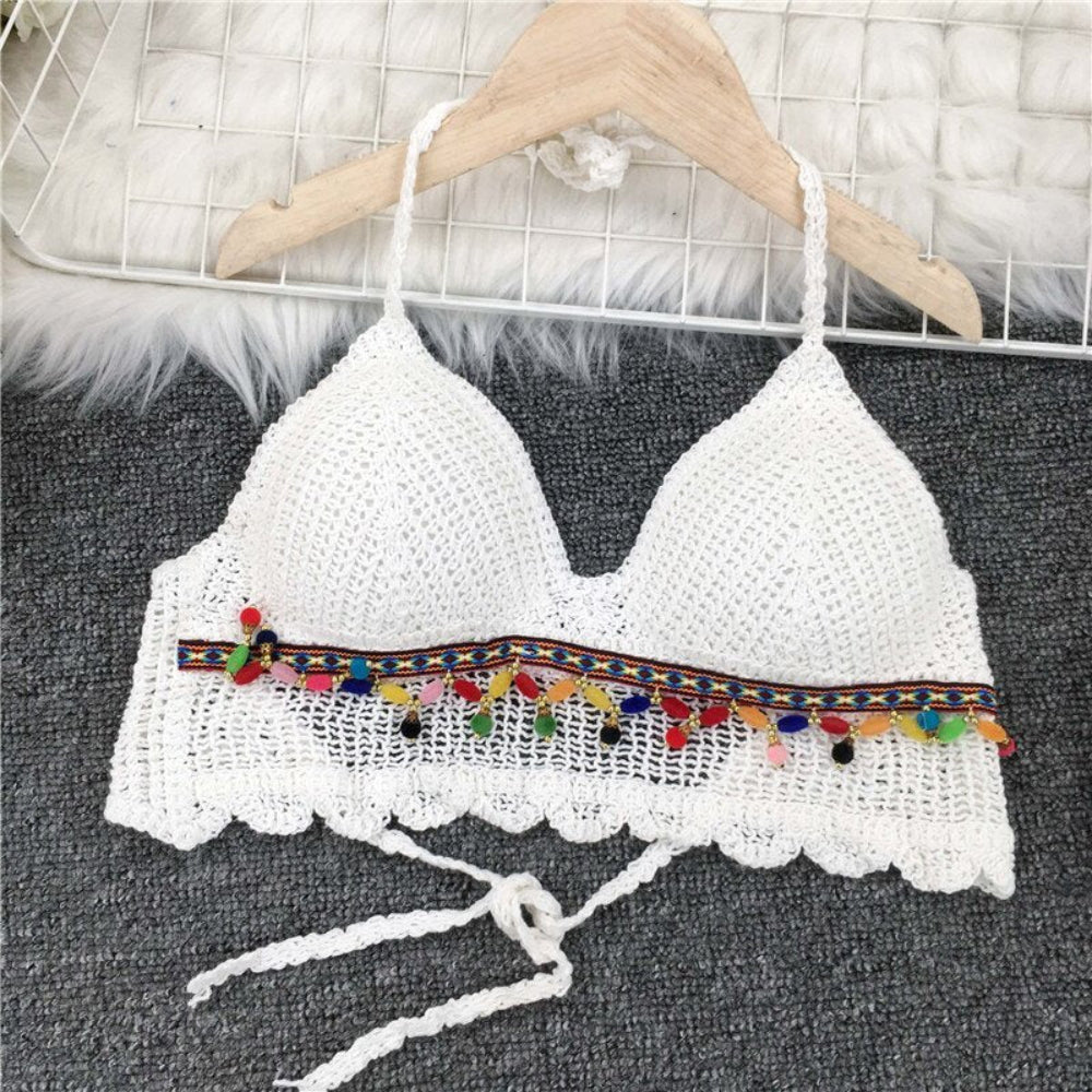 White crochet halter crop top with colorful pom pom trim hanging on wooden hanger