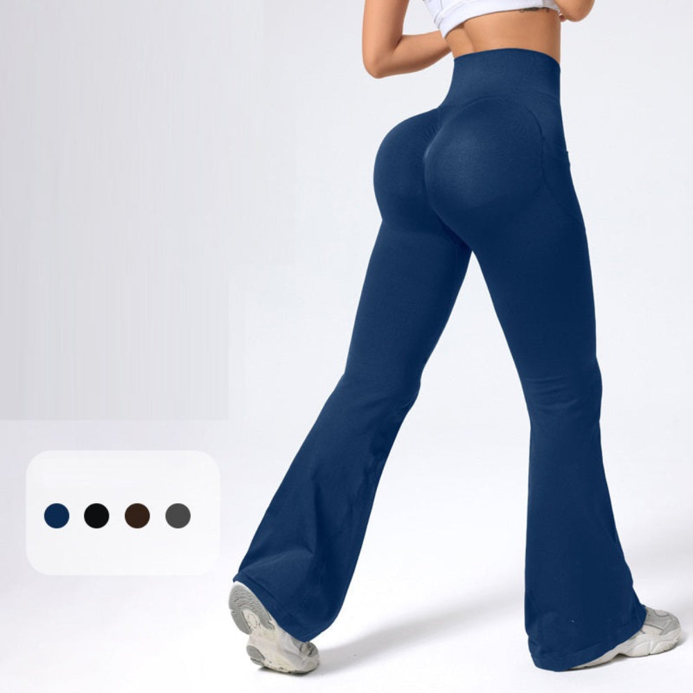 Woman modeling navy blue high-waisted flared pants with a flattering wide-leg silhouette, shown from a rear three-quarter view. Paired with a white crop top and sneakers against a clean white studio background
