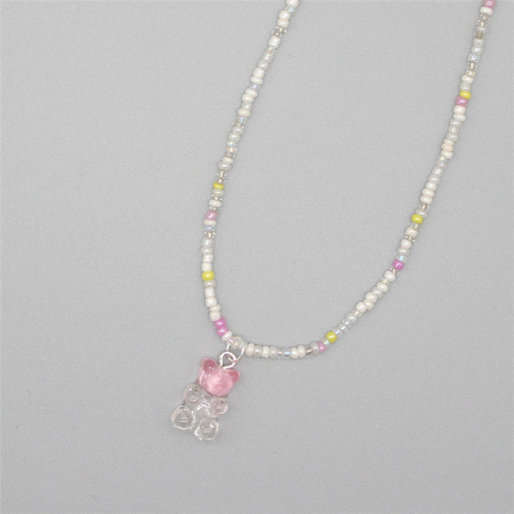 Delicate beaded necklace made with white pearl-like seed beads, iridescent clear beads, and pops of pink, yellow, and purple. Features a translucent pink gummy bear pendant. The dainty single-strand necklace is laid flat on a light gray background, showcasing its soft, whimsical style.