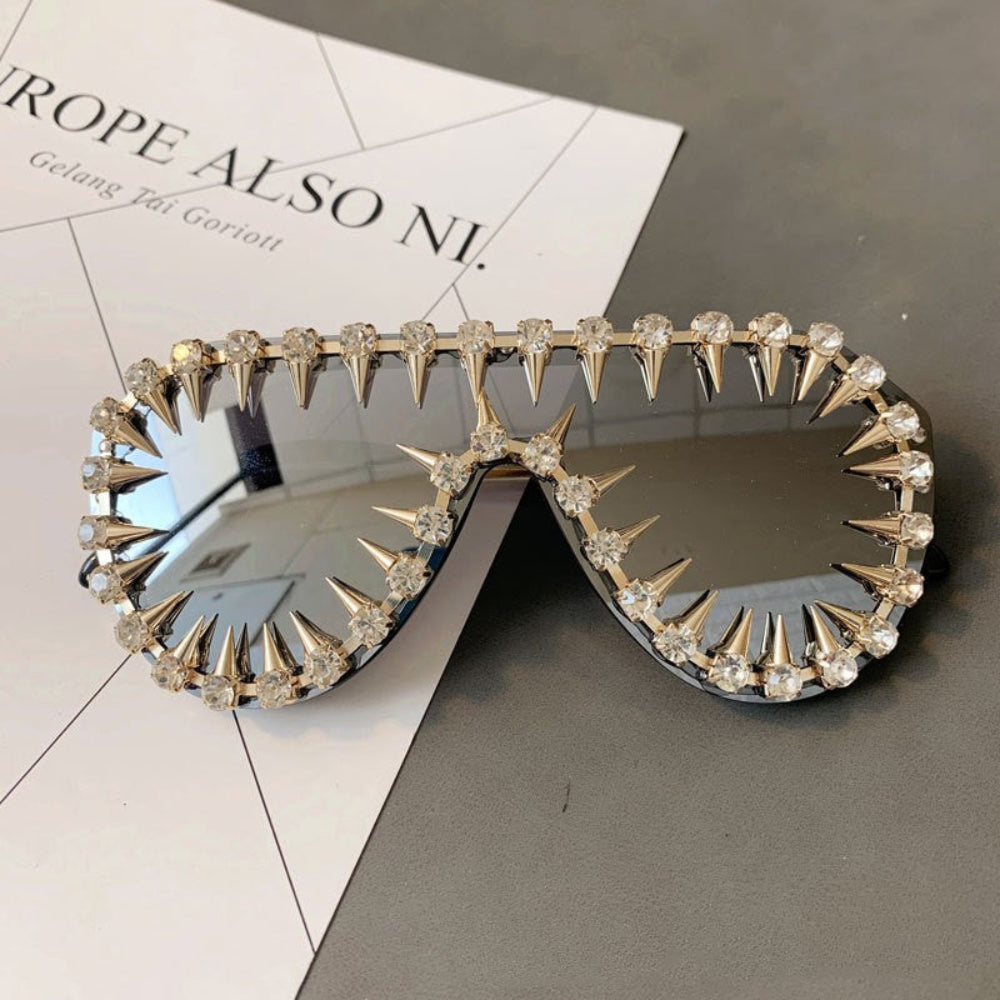 Gold spike crystal sunglasses – trendy designer statement sunnies with spikes and rhinestones, product flat lay on magazine.