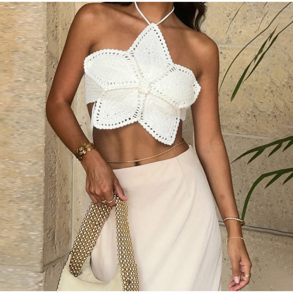 Model wearing a white crochet halter crop top with intricate floral butterfly design, paired with a beige skirt and gold chain accessories.