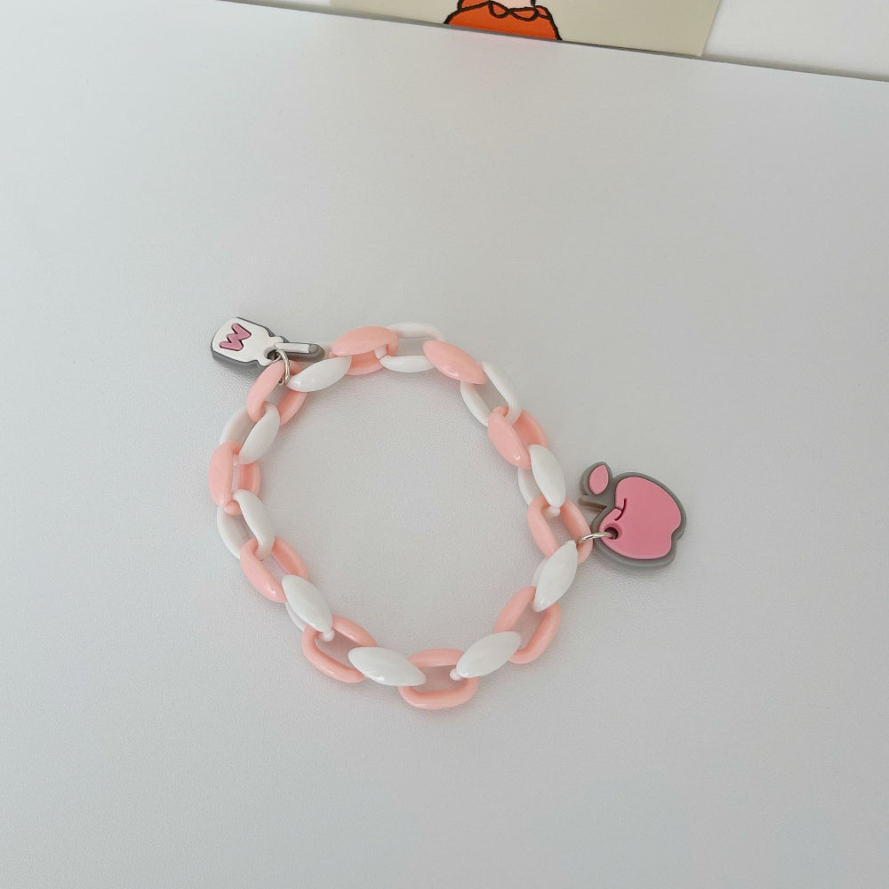 Pastel pink and white link chain bracelet featuring a pink bitten Apple logo charm and a white rectangular charm with pink "M" logo