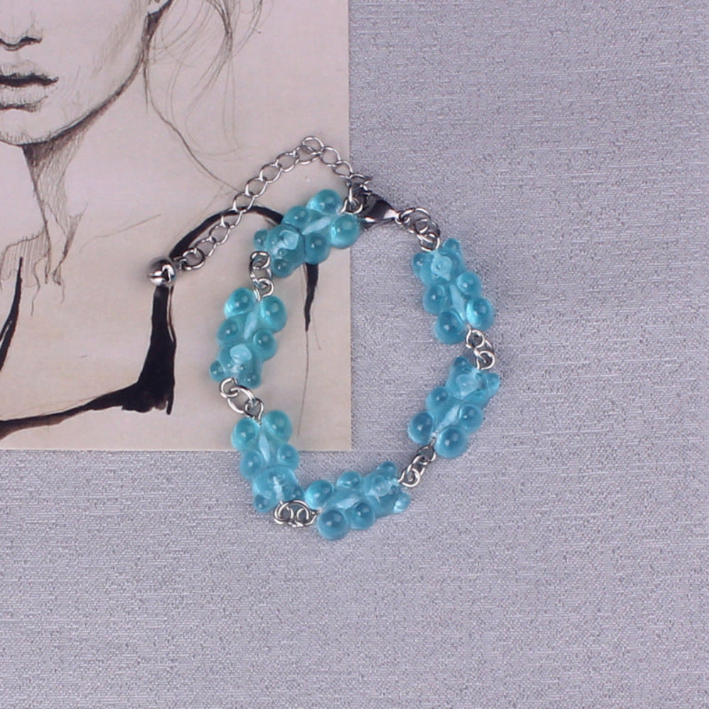 Blue gummy bear charm bracelet with silver metal chain, lobster clasp, and black tassel, featuring multiple translucent bright blue gummy bear charms, displayed on a textured background.