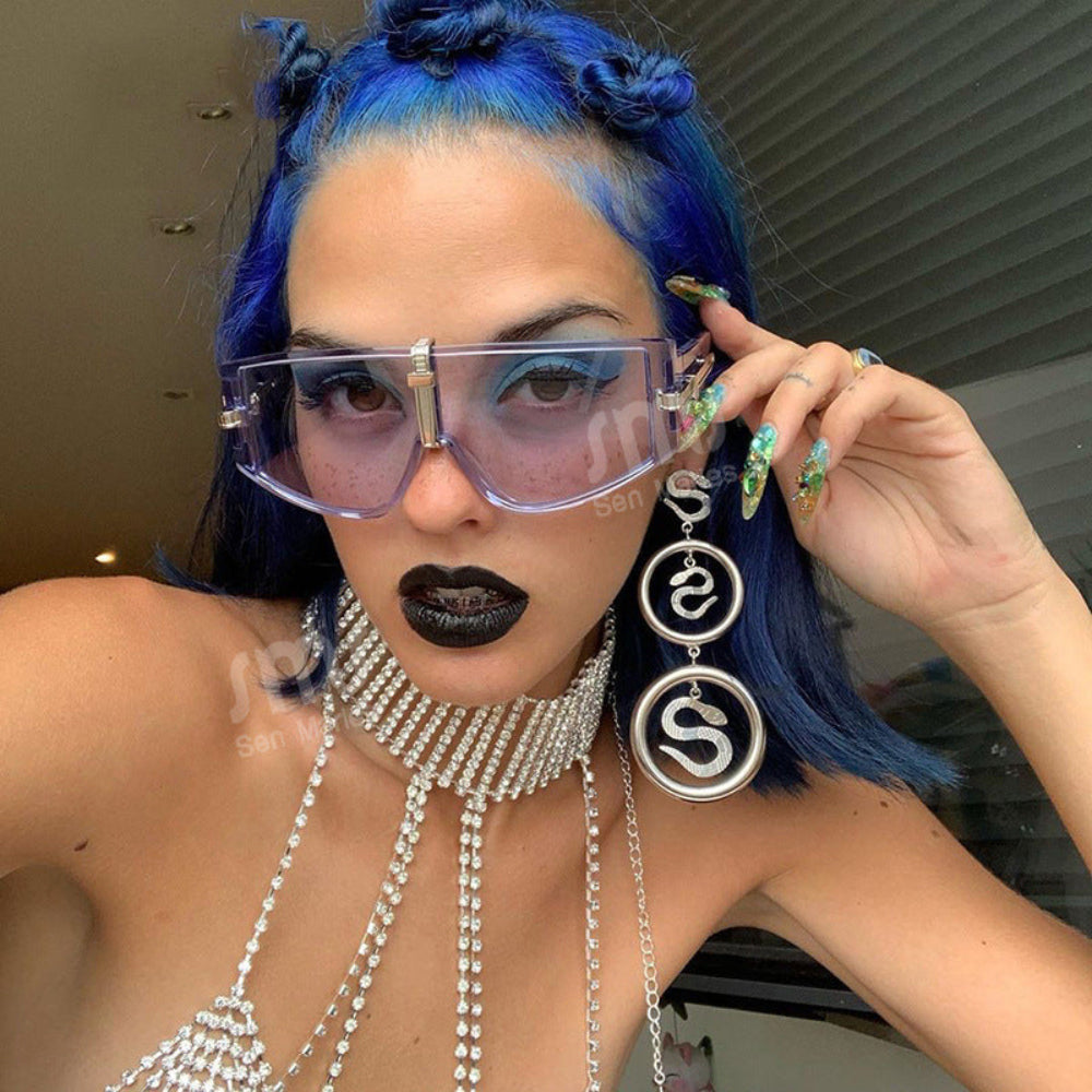 Translucent clear oversized shield sunglasses with silver center bridge, worn by model with blue hair