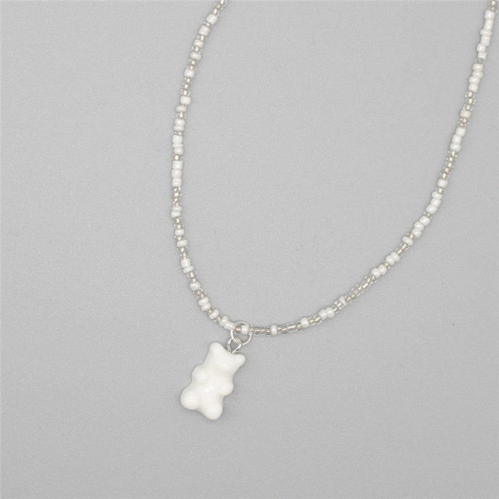 Minimalist white beaded necklace with a mix of white and silver seed beads paired with an opaque white gummy bear pendant. Delicate single-strand design laid flat on a light gray background, offering a clean, sweet, and versatile everyday look