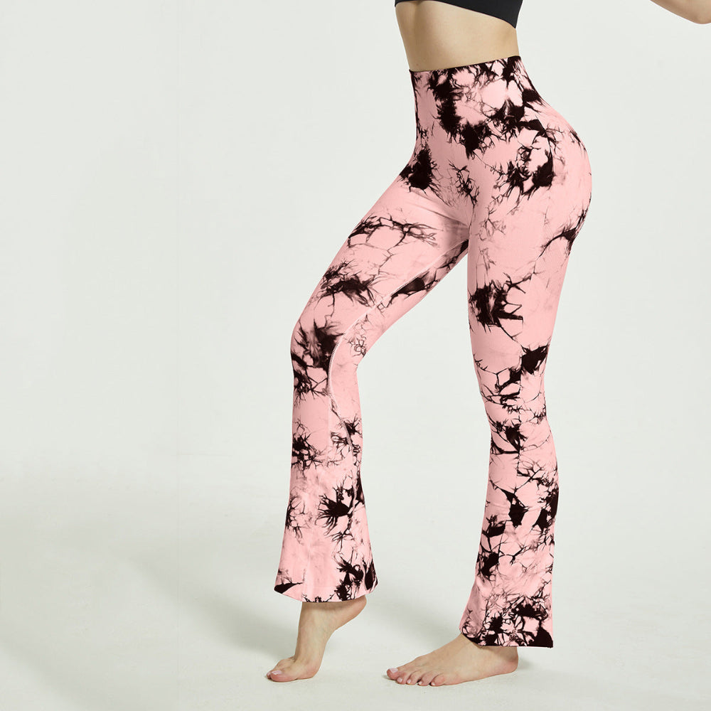 Woman modeling pink and black tie-dye high-waisted flared pants, shown from a side view while standing barefoot against a clean white studio background.