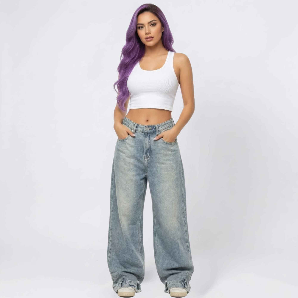 Full-length front view of a woman with long vibrant purple wavy hair modeling a casual outfit featuring a white ribbed sleeveless crop top and high-waisted light-wash wide-leg baggy jeans with a relaxed oversized fit. She stands with both hands in her front pockets against a plain white background.