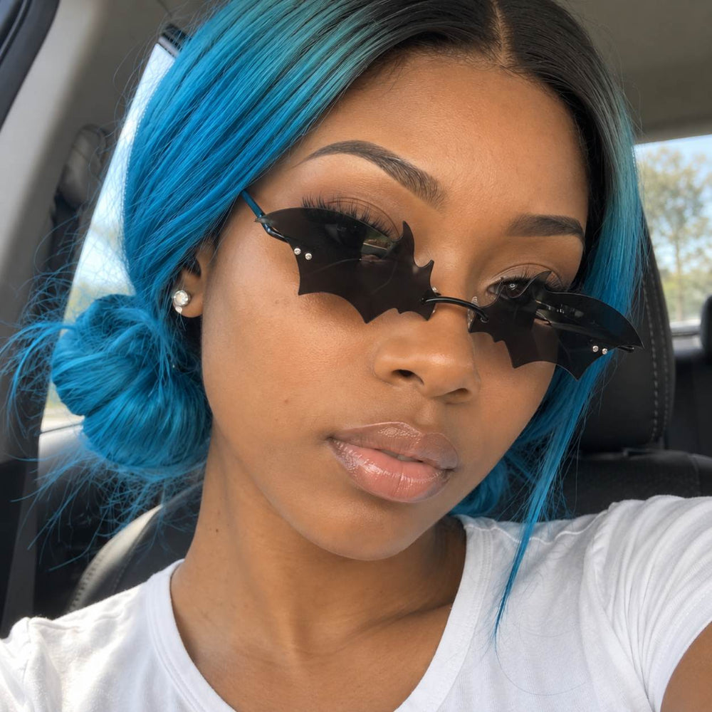 Woman with blue hair wearing rimless black bat-wing sunglasses.