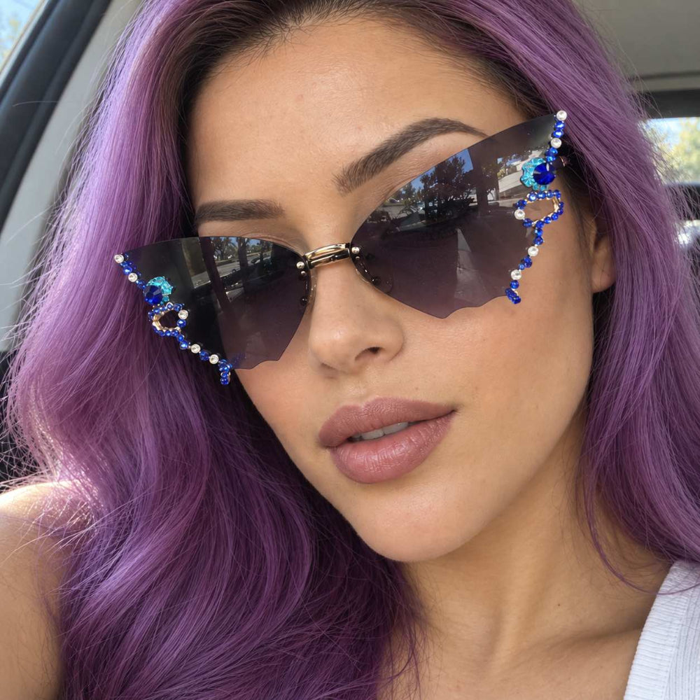 Woman with purple hair wearing rimless butterfly sunglasses with blue jewels and dark gradient lenses.