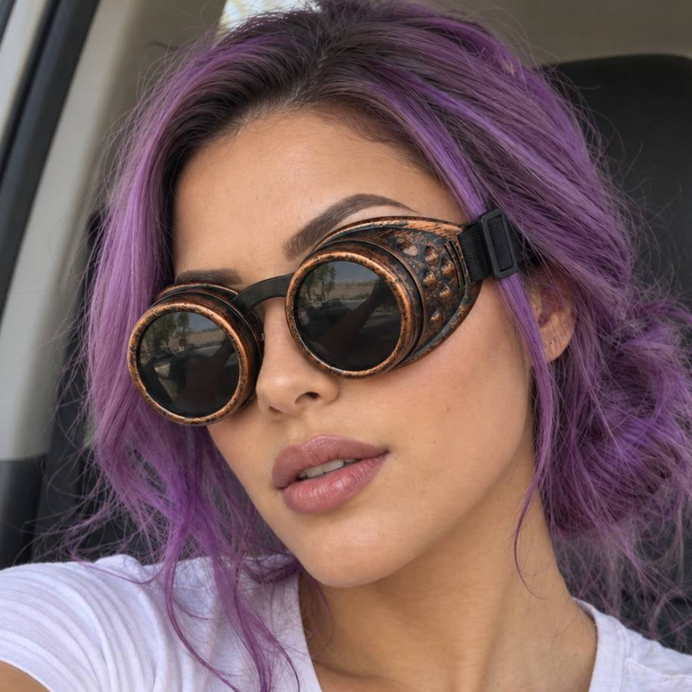 Woman with purple hair wearing bronze steampunk welding goggles with dark round lenses and a black strap.