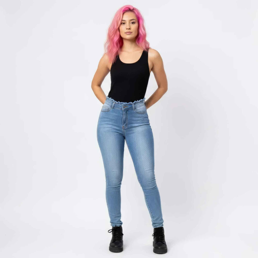 Full-length front view of a woman with vibrant pink hair modeling high-waisted light-wash skinny jeans with a frayed waistband detail. She is wearing a black sleeveless bodysuit and black combat boots, posing with hands in her pockets against a plain white background.