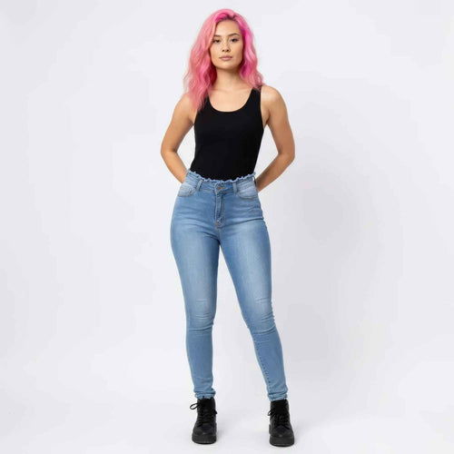 Full-length front view of a woman with vibrant pink hair modeling high-waisted light-wash skinny jeans with a frayed waistband detail. She is wearing a black sleeveless bodysuit and black combat boots, posing with hands in her pockets against a plain white background.