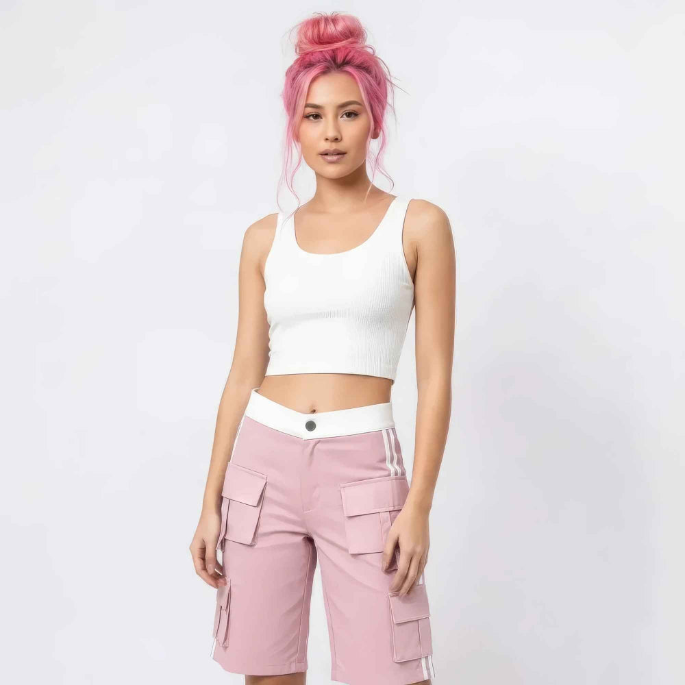 Woman with vibrant pink hair in a high bun modeling a white ribbed sleeveless crop top and pink cargo shorts with multiple pockets and white side stripes. Full-body studio shot for Boutique Jolie fashion collection.