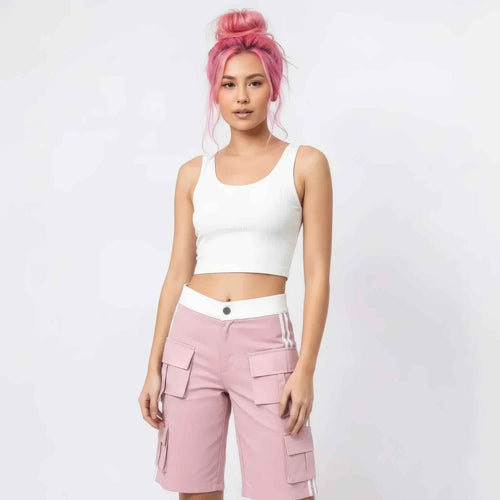 Woman with vibrant pink hair in a high bun modeling a white ribbed sleeveless crop top and pink cargo shorts with multiple pockets and white side stripes. Full-body studio shot for Boutique Jolie fashion collection.