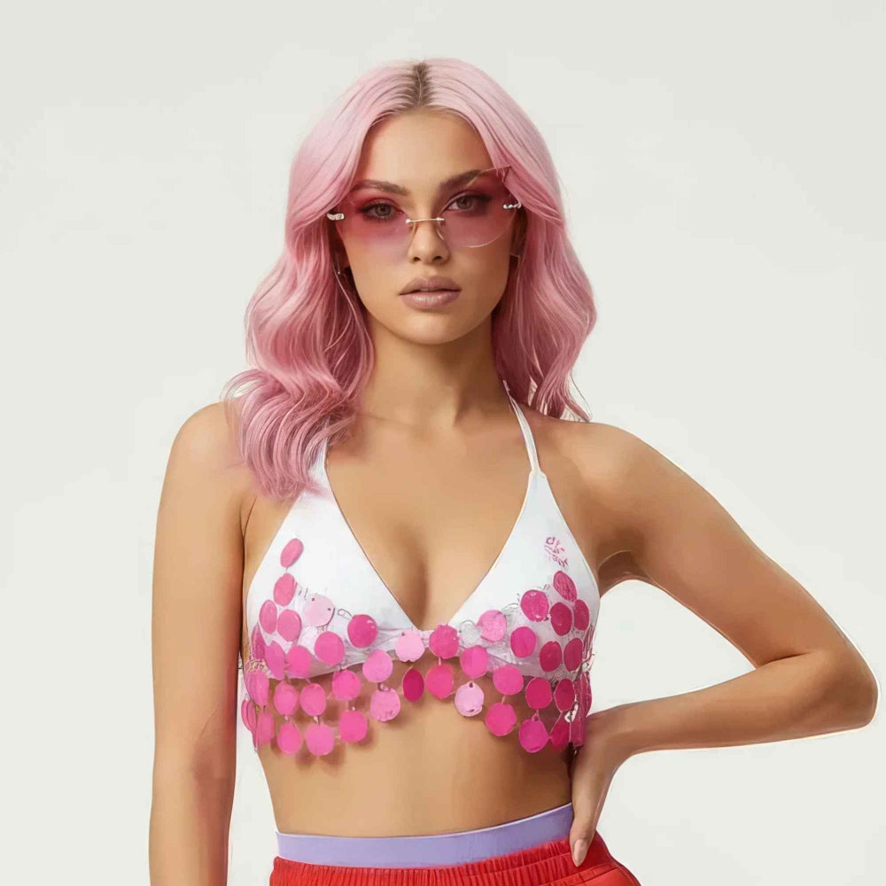 Woman with long wavy pink hair wearing pink-tinted rimless sunglasses and a white halter triangle crop top adorned with shimmering pink sequin discs. The playful sequin-embellished top is paired with red bottoms featuring a purple waistband, creating a bold and glamorous summer look.