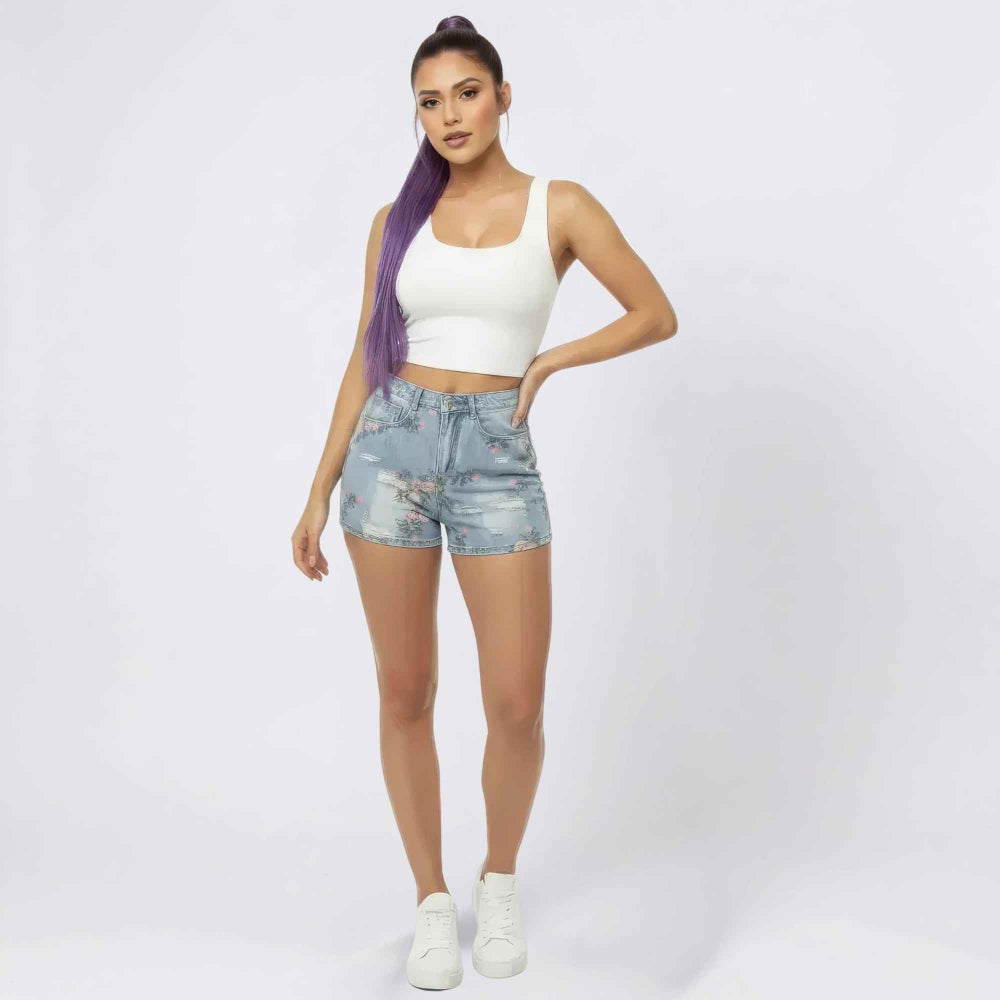 Woman with long purple hair in a high ponytail modeling a white sleeveless crop top and light blue floral embroidered denim shorts, styled with white sneakers. Full-body studio shot for Boutique Jolie fashion collection.