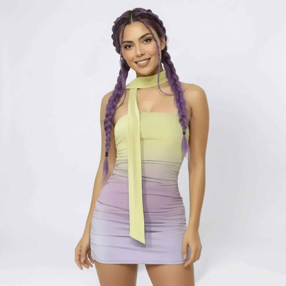 Front view of a woman with vibrant purple hair styled in two long braids smiling at the camera. She is wearing a form-fitting pastel ombre mini dress in yellow-to-lavender tones with a halter neck tie detail and ruched fabric, showcasing a flattering bodycon silhouette.