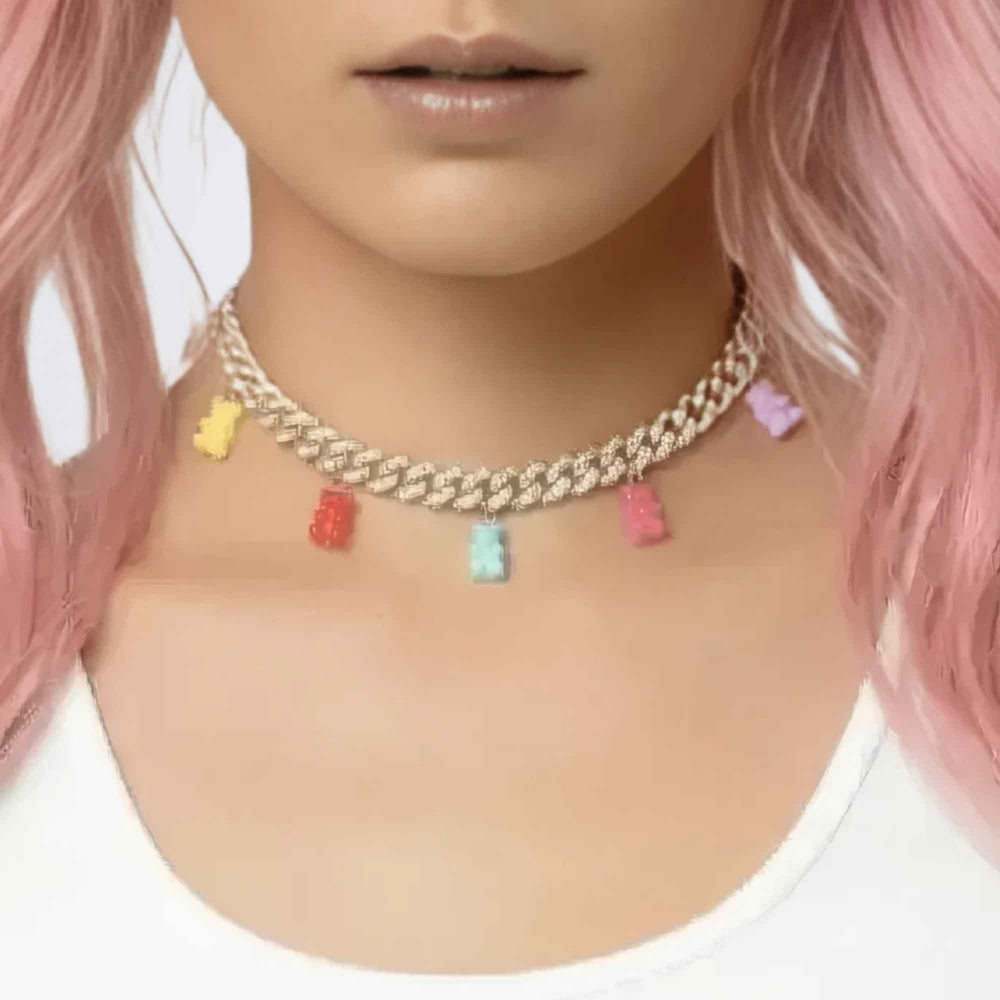 Close-up of a person with vibrant pink hair wearing a chunky gold curb chain choker necklace adorned with colorful gummy bear charms in yellow, red, blue, and pink.