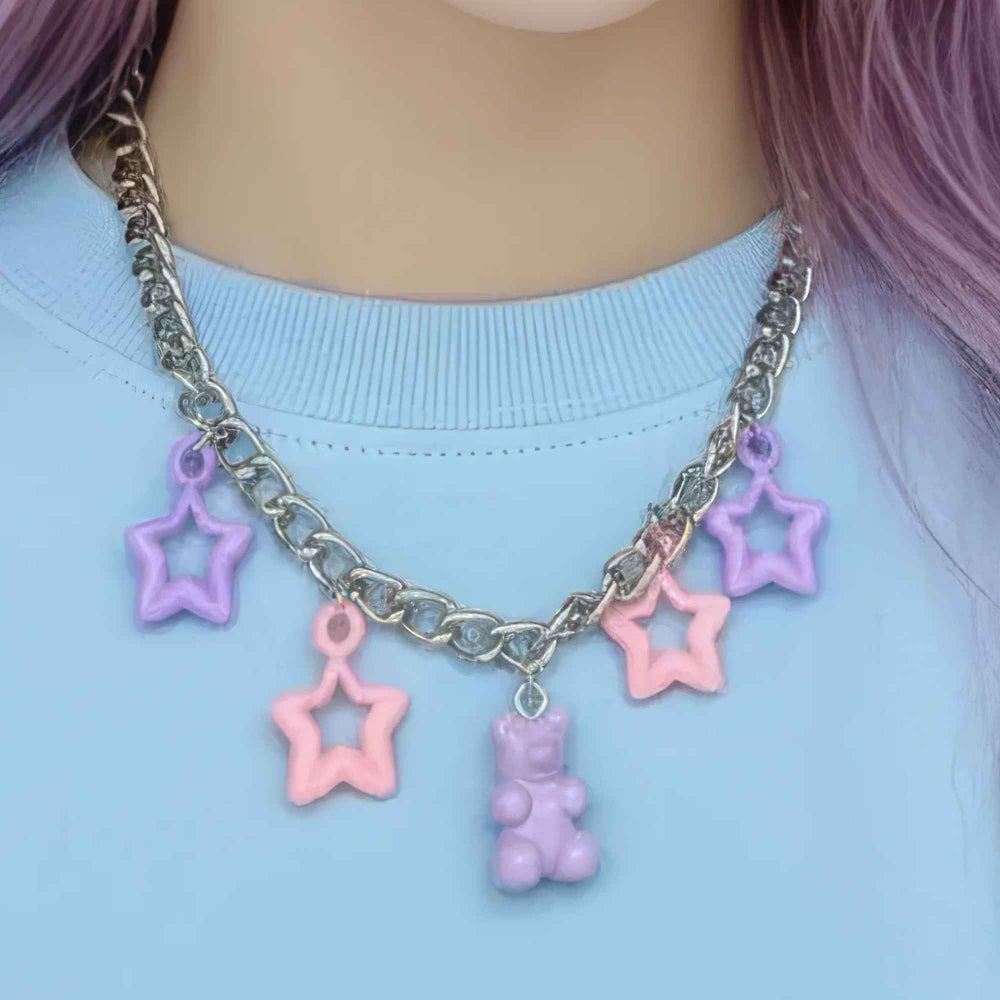 "Silver chain necklace with colorful star charms and a purple gummy bear pendant, worn with a light blue top"