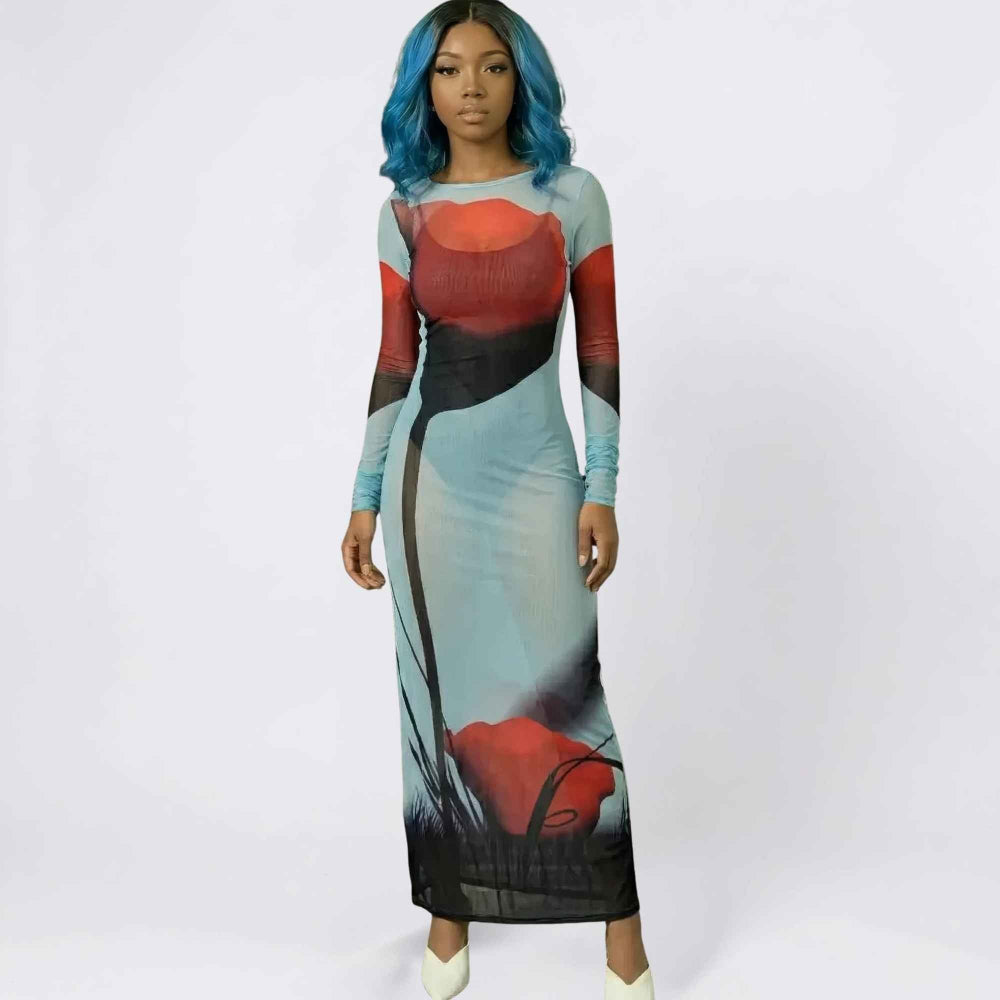 Full-length front view of a woman with vibrant blue wavy hair modeling a sheer long-sleeve maxi dress. The form-fitting dress features a bold artistic color-block print with red, black, and light blue panels, including large floral and abstract designs, creating a stylish, semi-transparent look.