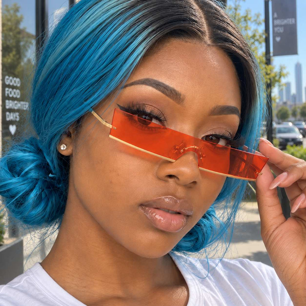 Woman with blue hair wearing rimless orange rectangular sunglasses.