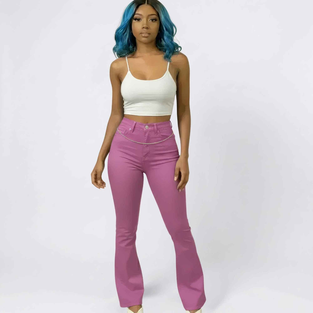 Full-length front view of a woman with vibrant blue wavy hair modeling a casual outfit featuring a white spaghetti strap crop top and high-waisted magenta flared pants. The pants have a flattering fit with a silver chain belt detail at the waist, styled for a trendy Y2K-inspired look.