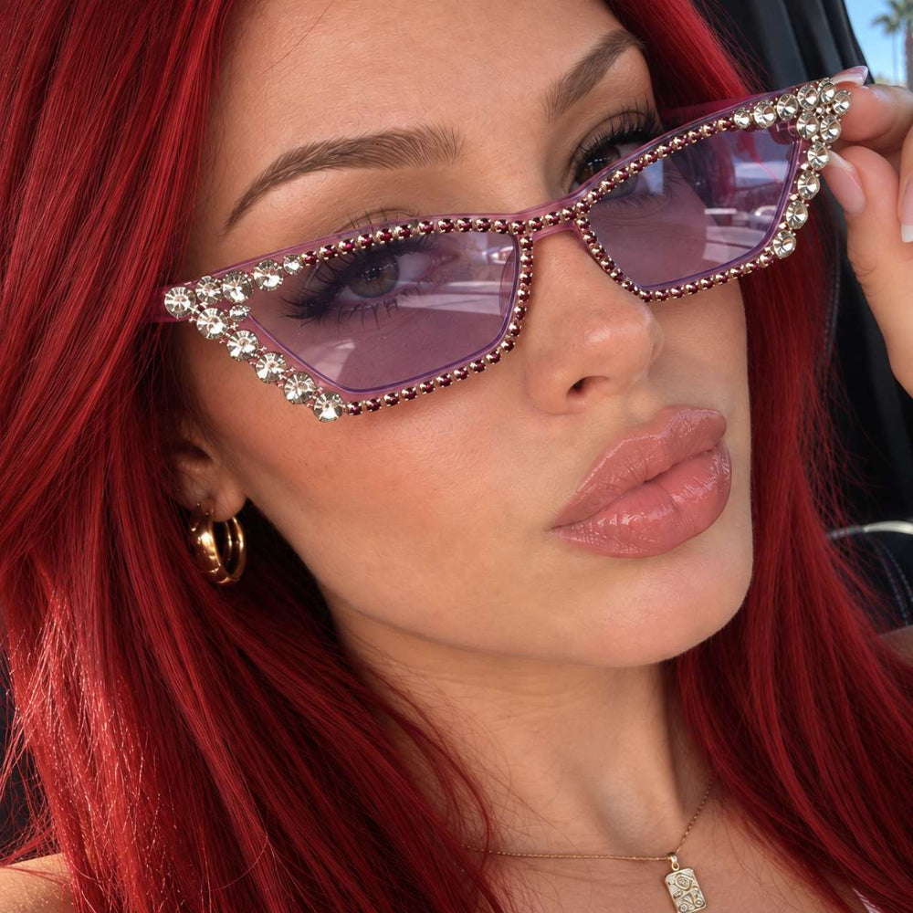 Woman with red hair wearing purple rhinestone cat-eye sunglasses with pink tinted lenses.