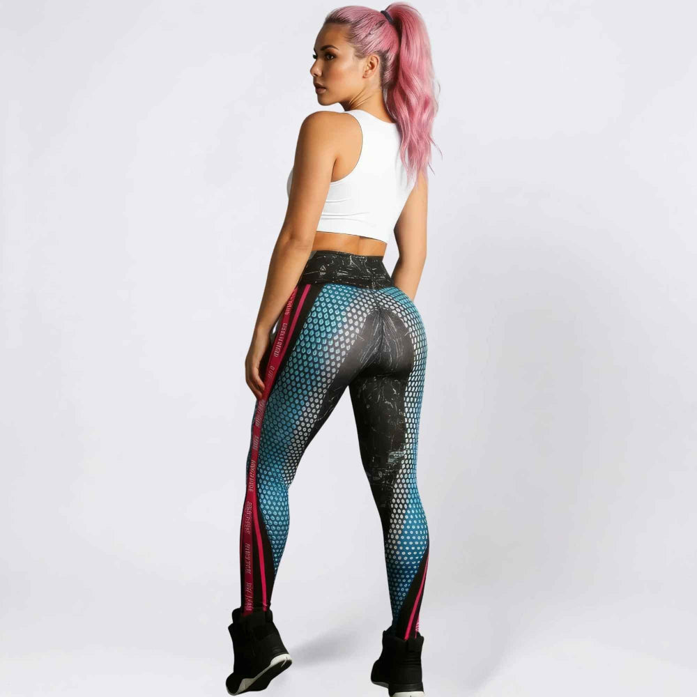 Back three-quarter view of a woman with bright pink ponytail hair modeling high-waisted leggings with a bold blue-to-black honeycomb pattern, pink side stripes, and textured detailing. She is wearing a white cropped tank top and black sneakers, posing to showcase the curve-enhancing fit in a studio setting.