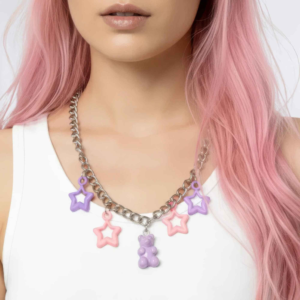Close-up of a person with long vibrant pink hair wearing a chunky silver curb chain necklace adorned with colorful star and gummy bear charms in shades of purple and pink, paired with a white tank top.
