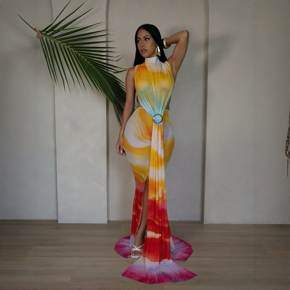 "Woman in a vibrant yellow, orange, and pink tie-dye gradient maxi dress with high slit and halter neckline, posing with a palm leaf in a minimalist studio"