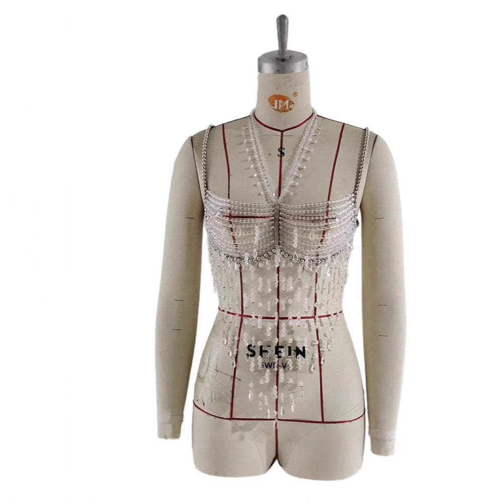 Mannequin displaying an elaborate silver beaded crop top featuring intricate pearl and chain embellishments, dangling bead strands, structured V-neckline, and multiple layers of sparkling details.