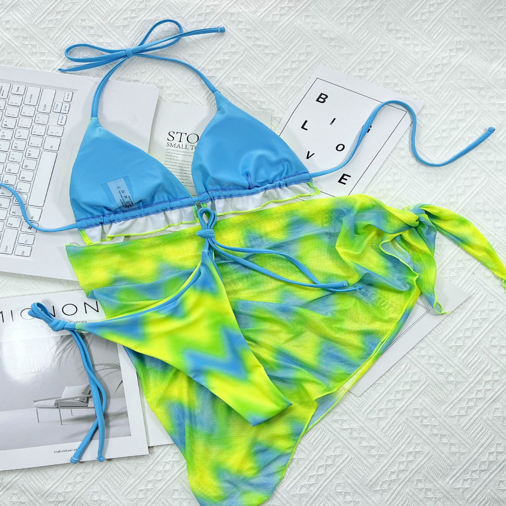 Blue and green tie-dye bikini set on a textured surface with magazines underneath.