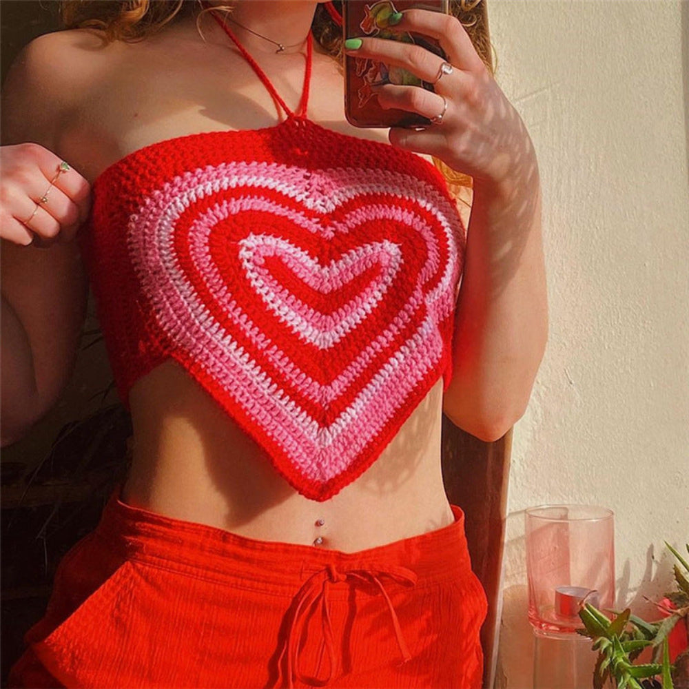 Young woman modeling a colorful red-to-pink ombre heart-shaped crochet halter top with red high-waisted shorts. She’s holding a phone for a mirror selfie, showing her midriff and belly button piercing.