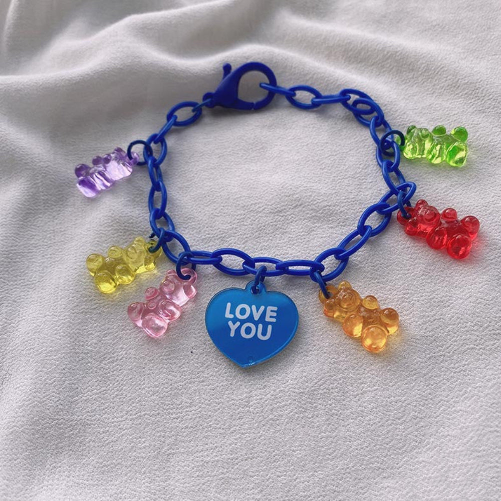 Blue gummy bear charm bracelet with a vibrant blue chain, featuring colorful translucent gummy bear charms in rainbow shades and a blue heart-shaped pendant engraved with "LOVE YOU", displayed on white fabric.