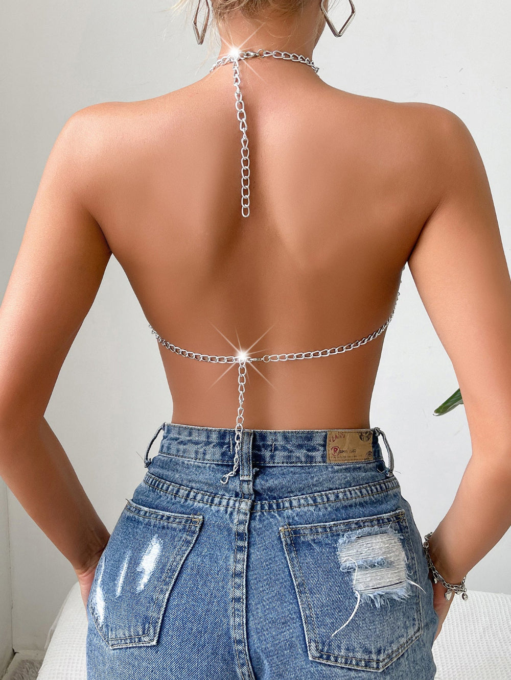 Silver chain halter body chain with dangling back detail, worn with distressed blue jeans, shown from the back on a model.