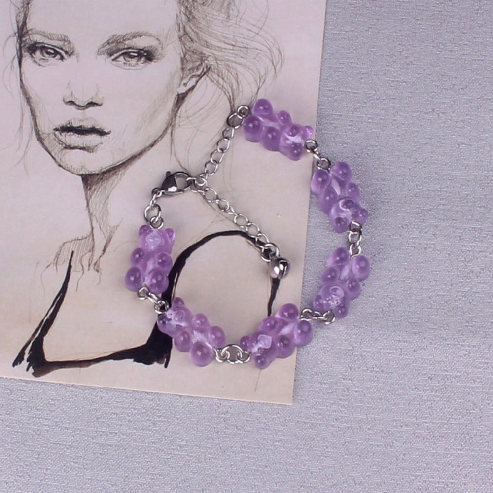 Purple gummy bear charm bracelet with silver metal chain, lobster clasp, and black tassel, featuring multiple translucent bright purple gummy bear charms, displayed on a textured background.