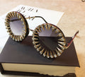 Black round steampunk sunglasses with gold spikes, rhinestones, and dark gradient lenses, displayed on a brown box.