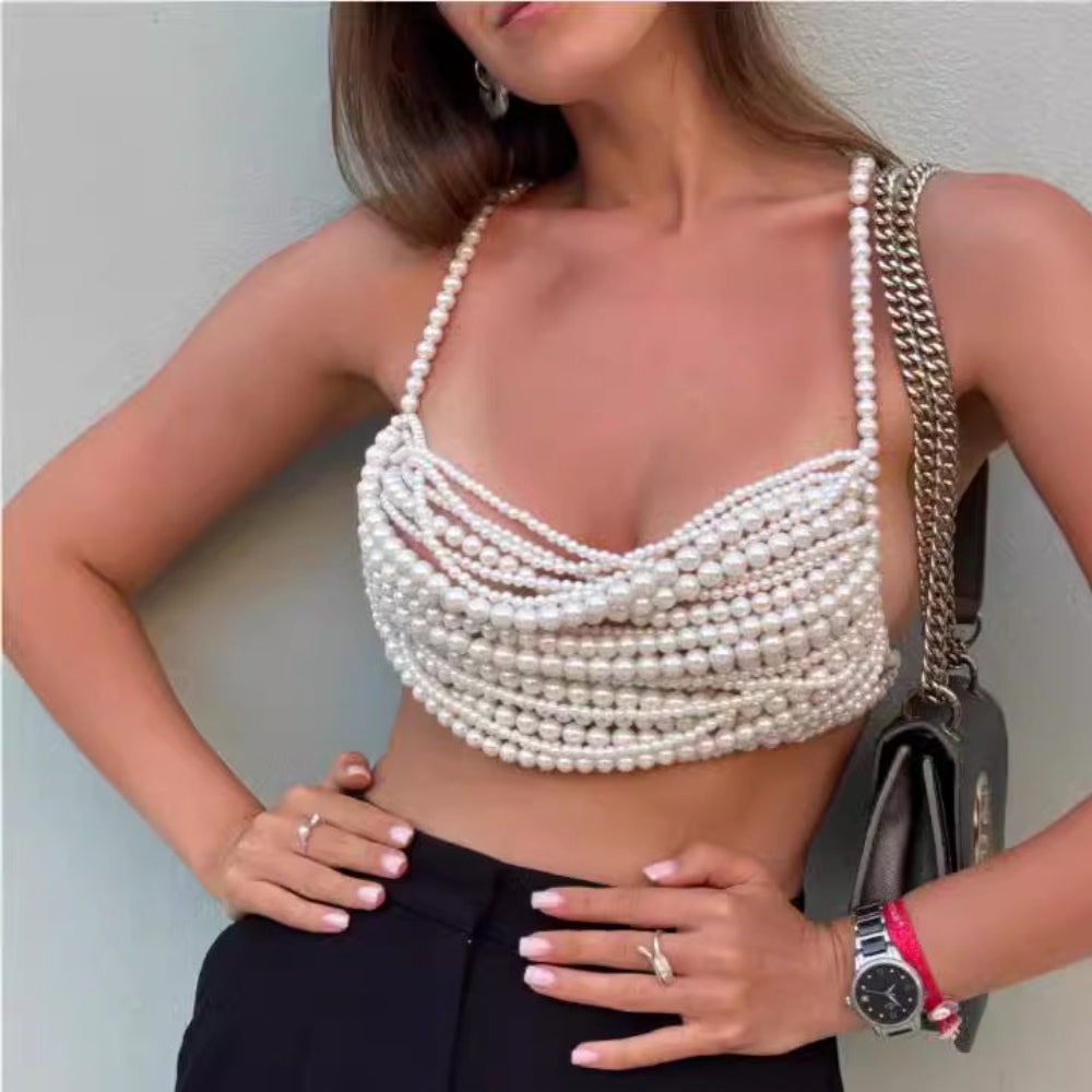 : A woman wearing a stunning multi-layered pearl crop top featuring dozens of horizontal white pearl strands that create a luxurious, woven effect across the bust and torso. Styled with black high-waisted trousers, a black chain-strap handbag, and accessories, posing confidently with hands on hips.