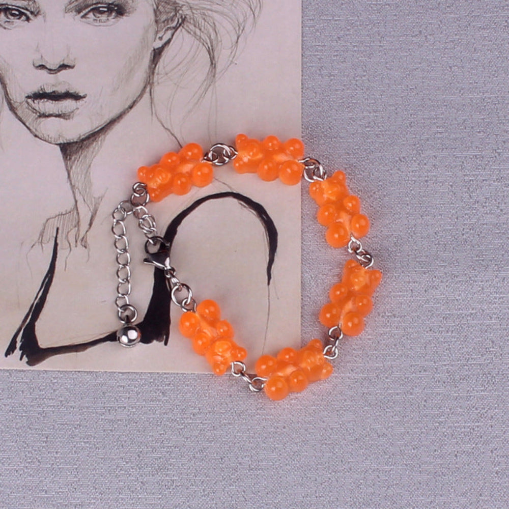 Orange gummy bear charm bracelet with silver metal chain, lobster clasp, and black tassel, featuring multiple translucent bright orange gummy bear charms, displayed on a textured background.