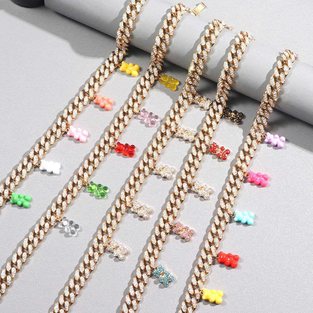 Luxury gold Cuban link choker necklaces fully iced with cubic zirconia stones, each adorned with colorful translucent gummy bear charms in white, green, pink, red, yellow, purple, black, and more. Bold statement jewelry collection displayed on a neutral surface.