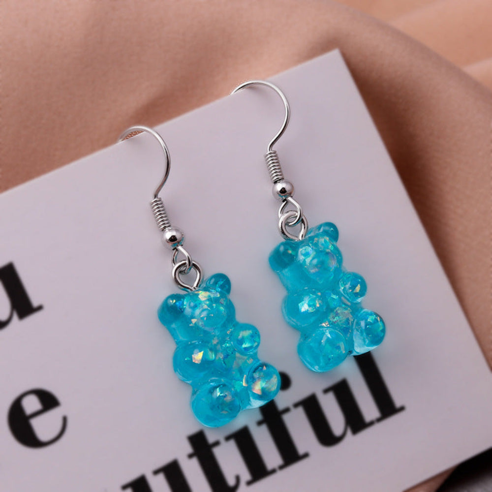 Pair of translucent blue gummy bear earrings with shiny silver fish hook ear wires and coiled ball connectors. Fun novelty resin teddy bear dangle earrings in vibrant turquoise blue.