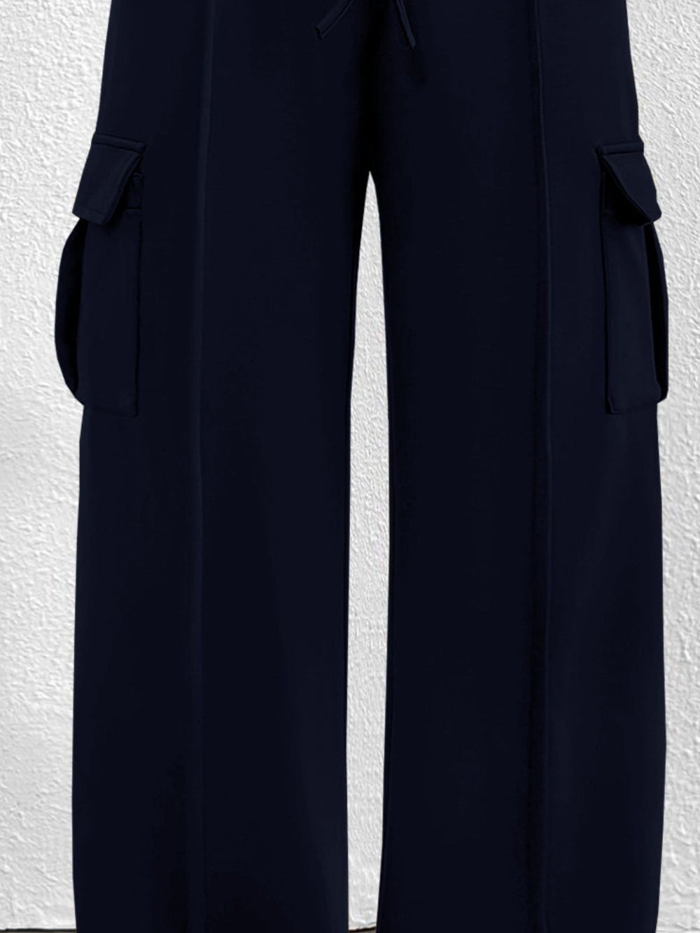 Navy blue wide leg cargo pants with large side pockets and drawstring waist against a textured white background