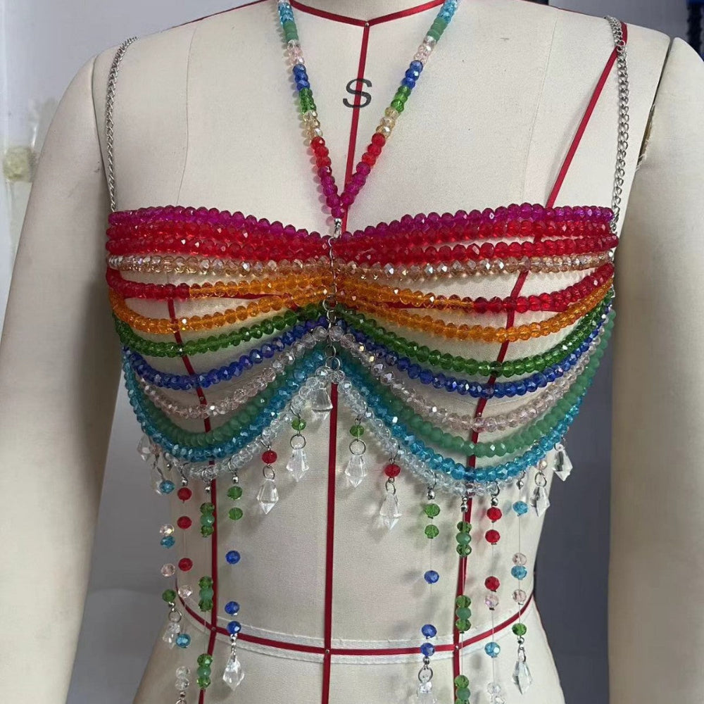 Mannequin displaying a vibrant rainbow beaded halter crop top featuring multiple layers of colorful beads in red, orange, yellow, green, blue, and purple. Includes cascading fringe with dangling crystal charms and beaded straps.