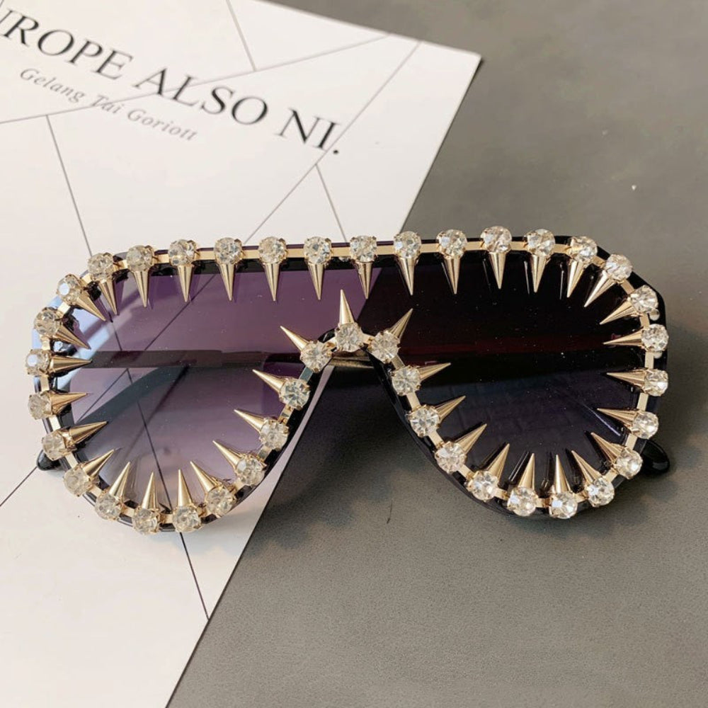 Gold spiked sunglasses with crystal embellishments resting on a fashion magazine page.
