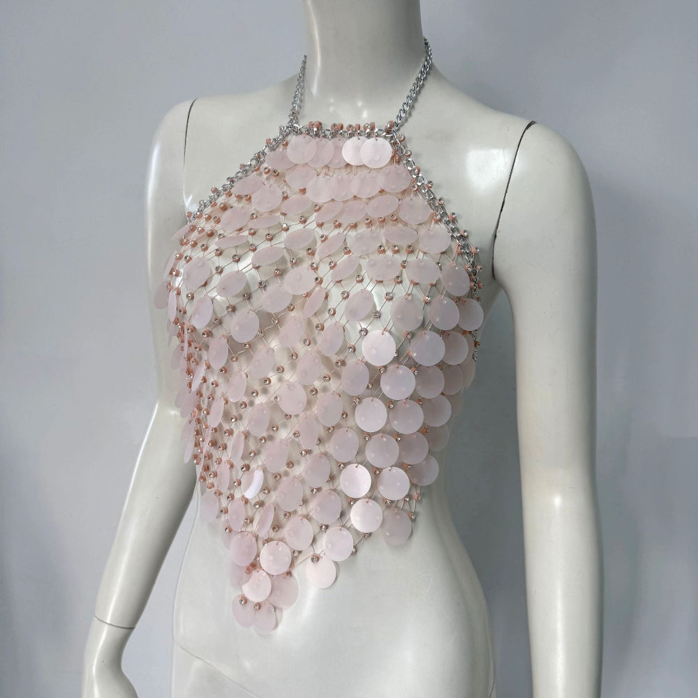 Mannequin wearing an elegant pale pink halter top composed of cascading layers of iridescent circular sequins, accented with silver chain straps and delicate bead details. The flowing, statement piece drapes beautifully across the torso.