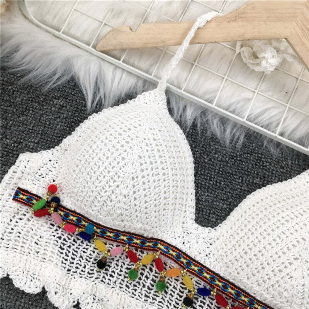 Close-up detail of white crochet halter crop top with colorful woven trim and pom poms.